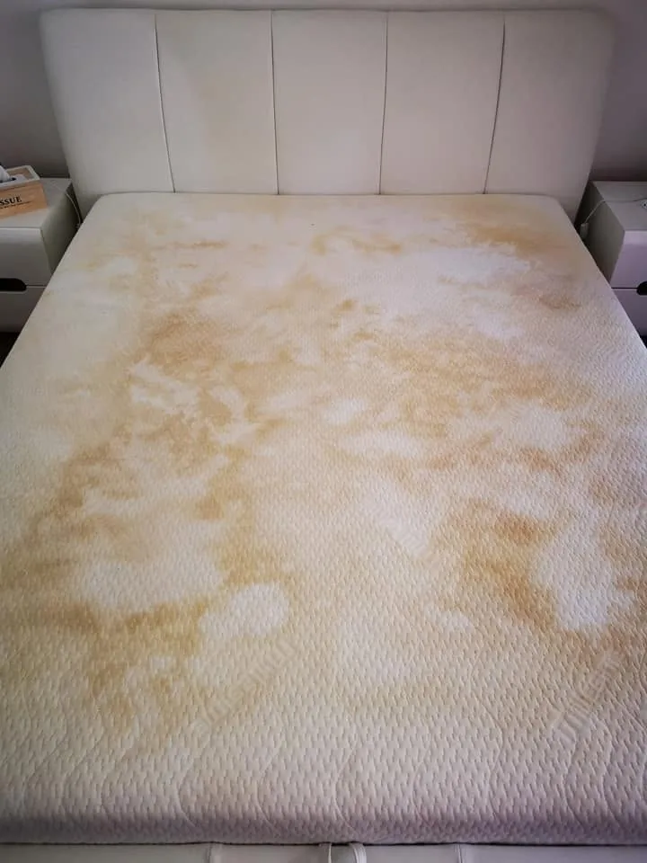 Textured mattress cover with widespread yellow-brown staining before cleaning