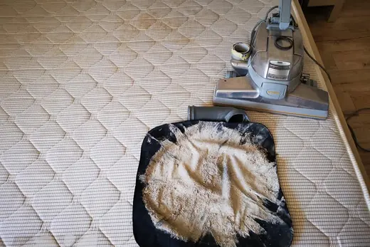 Collected dust and fibres on a dark cloth beside a mattress vacuum head
